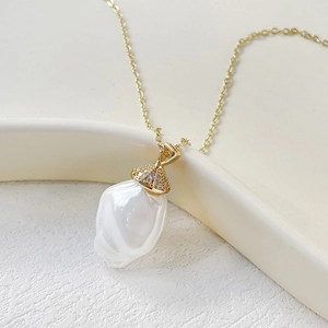 Collana con perla barocca e ciondolo dorato con zirconi su sfondo bianco morbido