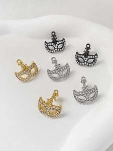 Dettaglio macro di ciondoli a maschera con zirconi in oro, argento e nero