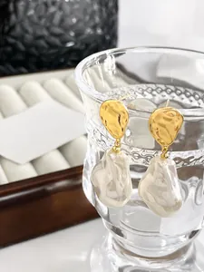 Detail von 18k vergoldeten Ohrringen mit Barockperlen an einem Glasrand hängend
