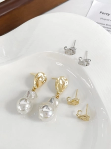 Details von 18 Karat vergoldeten geometrischen Ohrringen mit Barockperlen auf weißem Keramiktablett