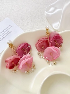 Detail of pink mesh fabric flower earrings with pearls and gold accents on a tray