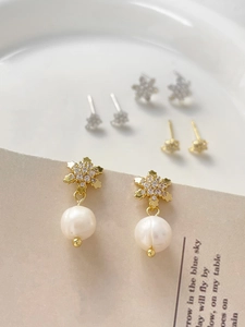 Close-up of gold-plated snowflake earrings with zircon inlay and elegant white pearls