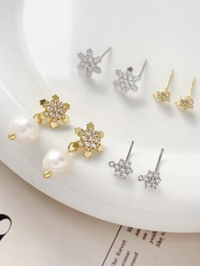 Detailed view of gold plated snowflake earrings with zircons and pearls on white ceramic