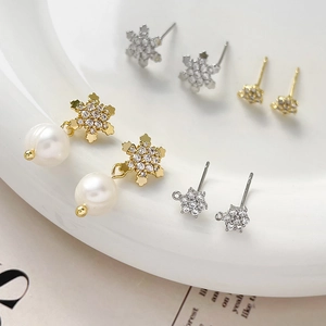 Gold-plated snowflake earrings with zircon inlay and pearls on a white porcelain plate