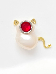 Vue macro d'une broche chat avec gemme rouge, oreilles dorées et base en perle