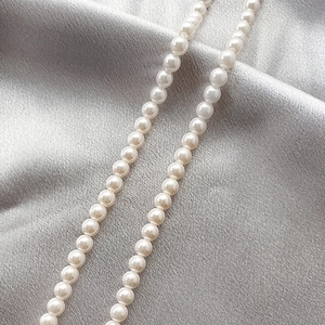 Close-up of white shell pearl strand showing glossy texture on grey satin background