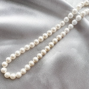 Close-up of glossy white shell pearls on silver silk fabric showing luxury texture