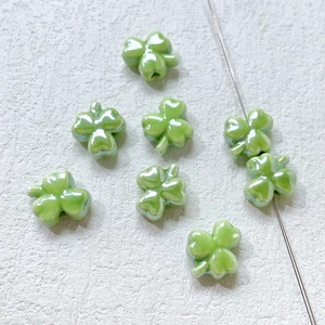Detailed view of light green ceramic clover beads with pearl finish on a white textured background