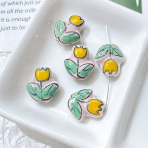 Macro shot of hand-painted ceramic tulip beads for DIY jewelry making in a white tray