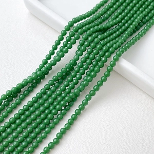 Gros plan de perles rondes en cristal vert vif disposées sur une surface en cuir blanc