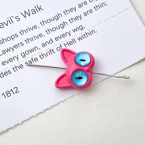 Macro shot of pink cat-shaped charm with blue eyes and metal needle on white card