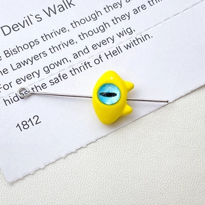 Macro detail of yellow cartoon monster eye bead for DIY jewelry on a metal needle