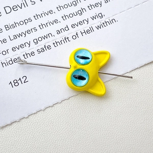 Macro shot of a yellow cartoon cat bead showing the perforation hole with a metal needle