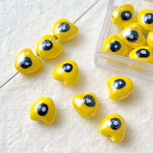 Detalle de cuentas de corazón de cerámica amarilla con ojo turco para joyería DIY