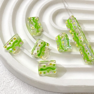 Macro shot of glass beads with green waves and pink dots on a ceramic plate