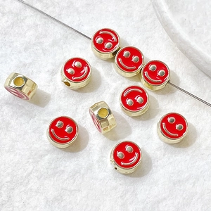 Detailed view of red enamel smiley face beads with gold frames for DIY jewelry making