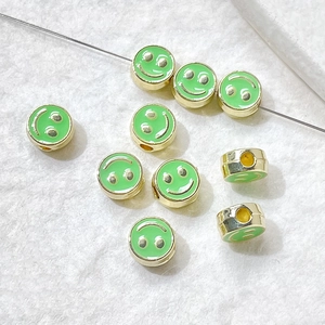 Detailed view of green enamel smiley face charms with gold base for DIY jewelry making
