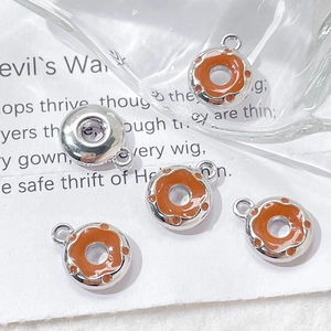Close-up of orange enamel donut charms for DIY jewelry making on white textured paper