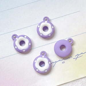 Makro-Detail von vier lila Donut-Anhängern für DIY-Schmuck auf Vintage-Papier