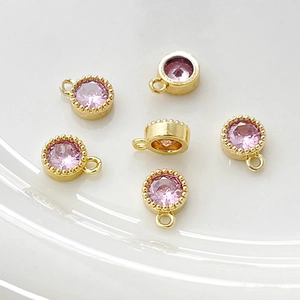 Detalle macro de 5 colgantes redondos de circón rosa bañados en oro con bordes milgrain para DIY