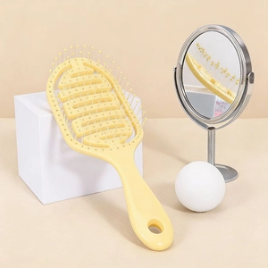 Pale yellow vented hairbrush for styling and scalp massage on a minimalist background