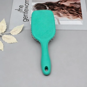 Mint green hairbrush with air cushion on a minimalist grey background with magazine