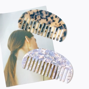 Gros plan de peignes en acétate écaille et marbre violet posés sur un magazine chic