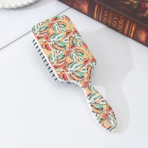 Detail of rectangular cushion hairbrush with tropical monstera leaf print and black massage pins