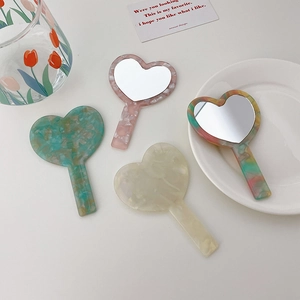 Elegant heart-shaped acetate handheld mirrors in multiple colors on a white desktop