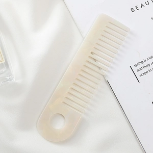 Close-up of cream marble pattern hair comb with wide teeth and round hanging hole design