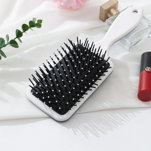 Minimalist white square paddle hairbrush with black massage pins on white fabric background