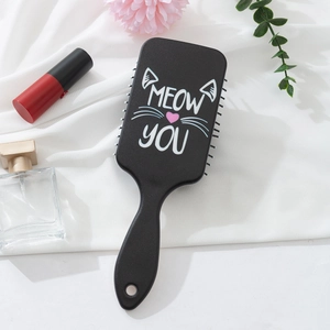 Detail of black rectangular hairbrush with cat motif and Meow You text on knit background
