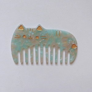 Detailed close-up of marble acetate cat hair comb with golden facial accents and ears