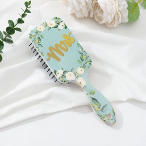 Close-up of floral air cushion hairbrush with gold Mrs lettering on light blue surface