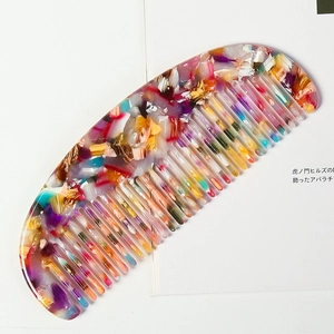 Close-up of a wide-tooth acetate comb with colorful marble pattern on a white page