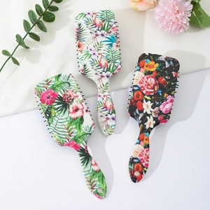 Three printed air cushion hair brushes with floral and flamingo patterns on bright background