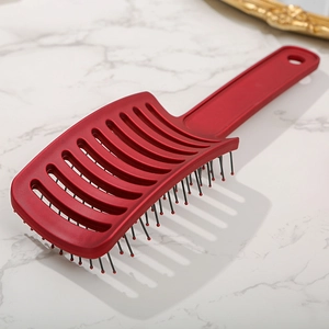 Curved vented hairbrush in deep red with massage tips on marble background