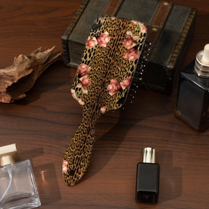 Detailansicht der Haarbürste mit Leopardenmuster und rosa Rosen auf einem Holztisch