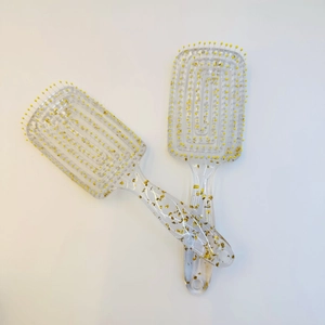 Detail view of two transparent hairbrushes with gold foil flakes and ball-tipped massage bristles