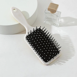 Détail d'une brosse à cheveux massante carrée avec manche beige sur fond minimaliste
