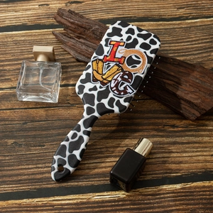 Détail de la brosse à cheveux motif vache avec broderie LOVE sur fond en bois sombre