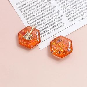 Dettaglio di un ciondolo esagonale in resina arancione con foglia d'oro, cristallo e chitarra