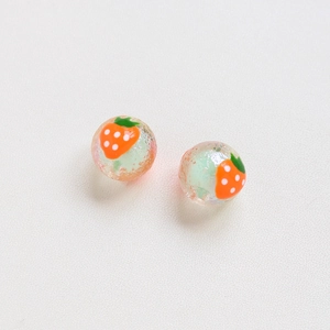 Macro detail of handmade strawberry glass beads for DIY jewelry with green core and red patterns
