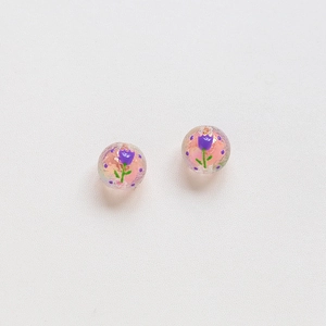 Macro detail of handmade round beads with hand-painted purple tulips and floral patterns