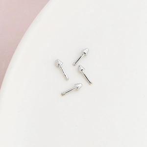 Macro detail of four silver screw-thread earring posts on a white ceramic plate