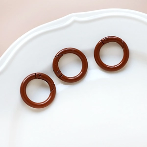 Three brown metal spring ring buckles on a white decorative plate for DIY crafts