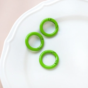 Three bright green circular spring ring clasps for DIY accessories in a white ceramic dish