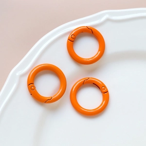 Three bright orange round spring O-rings for DIY keychains and jewelry on white plate