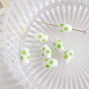 Close-up of white oval ceramic beads with green polka dots and a gold metal pin detail