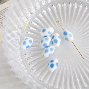 Macro view of white oval ceramic bead with blue polka dots and silver eye pin detail